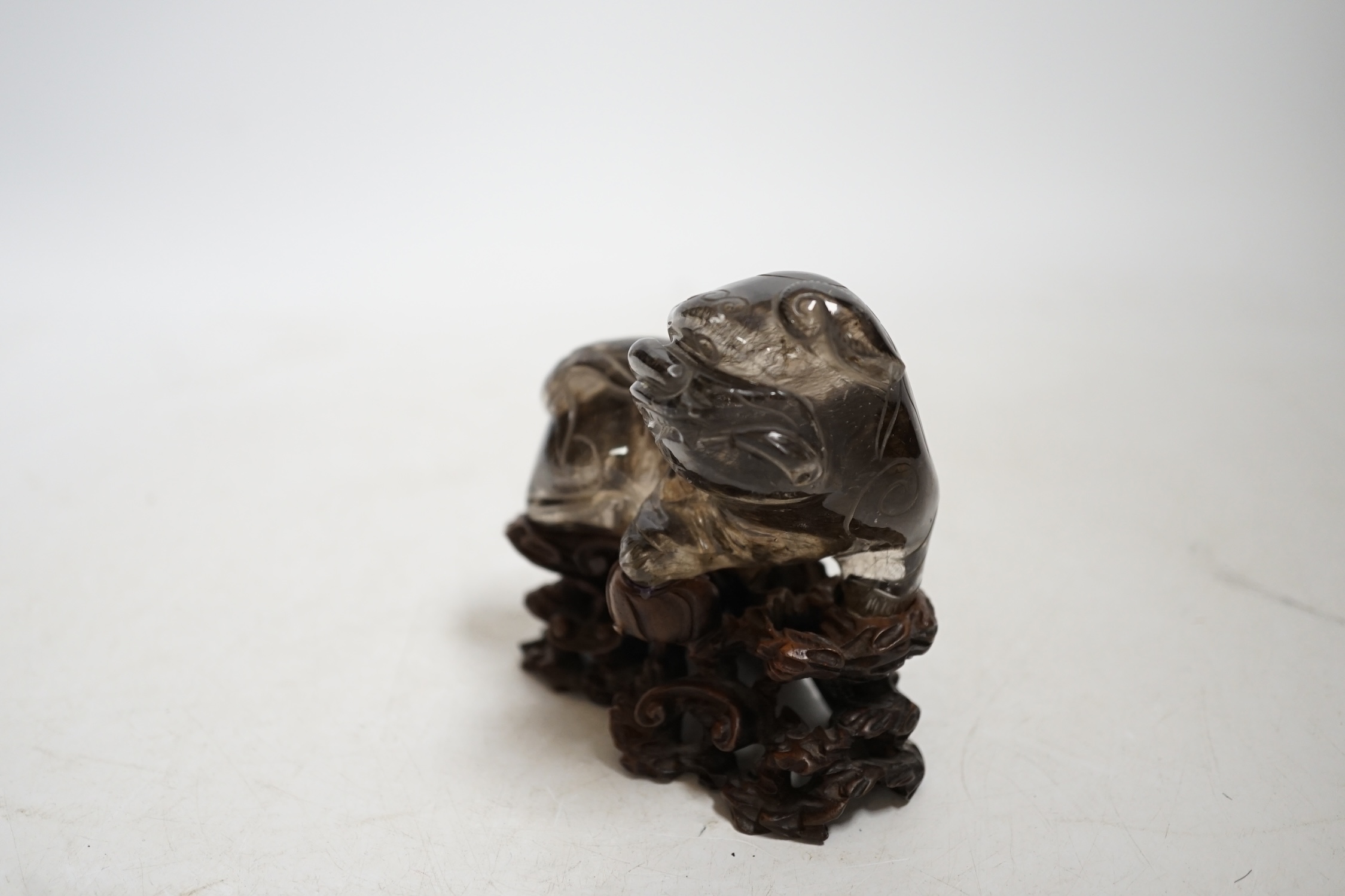 A Chinese carved smoky quartz lion dog on hardwood stand, 9.5cm wide. Condition - fair, impact damage to tail